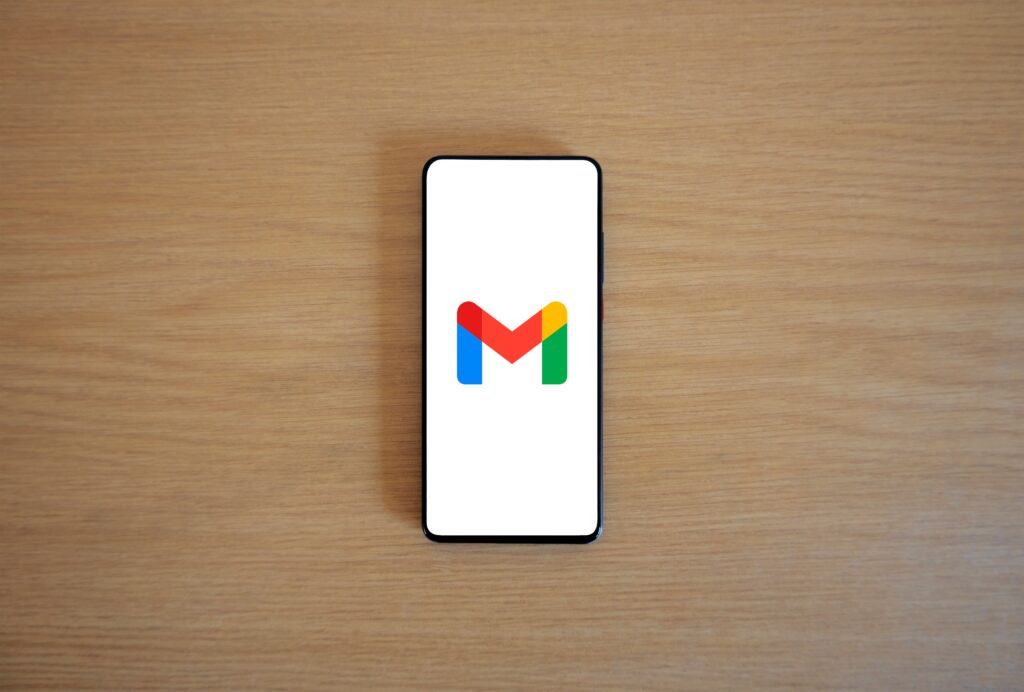 Logo de Gmail en pantalla de celular sobre mesa de madera, representando la gestión de correos electrónicos