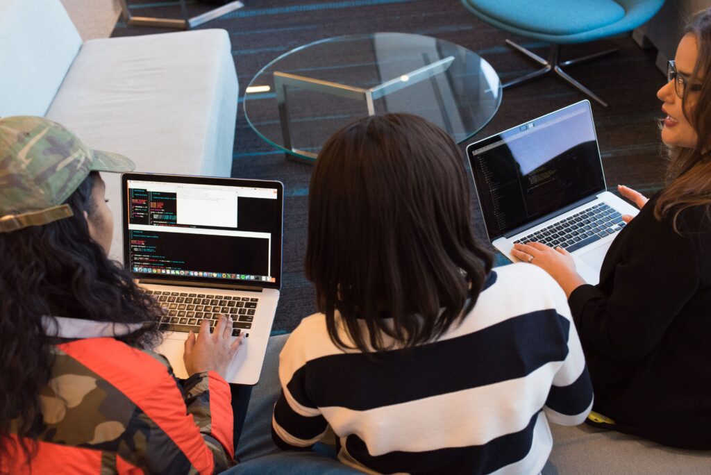 Tres personas trabajando juntas con laptops mostrando código de programación en un espacio de oficina